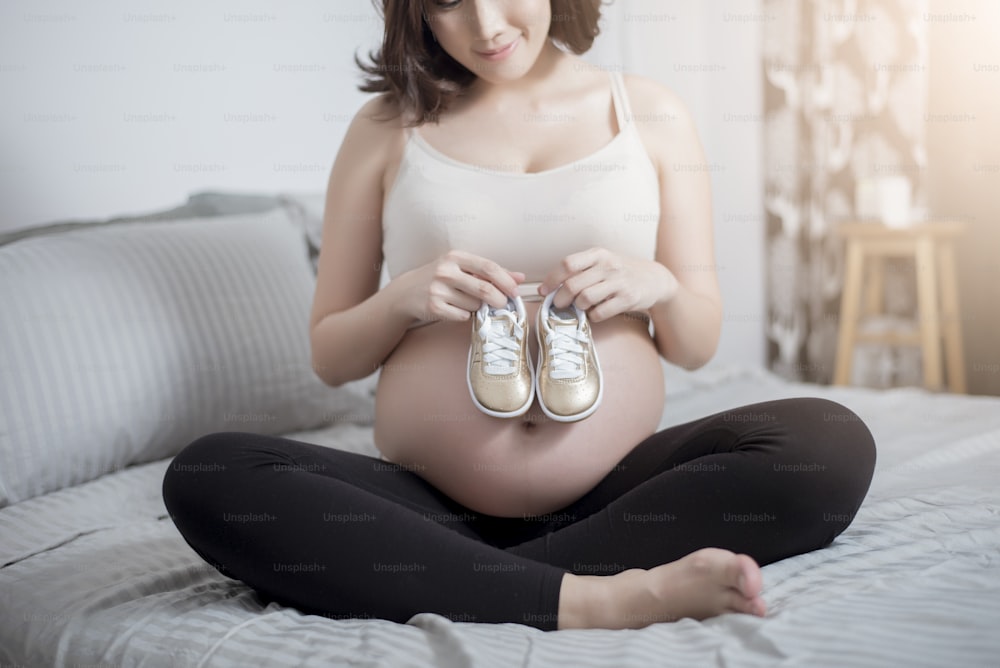 Beautiful asian pregnant woman expecting her baby with small shoes