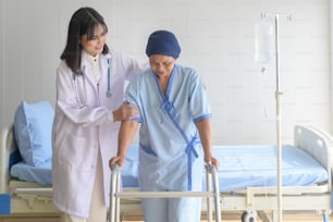 Doctor helping cancer patient woman wearing head scarf with walker at hospital, health care and medical concept