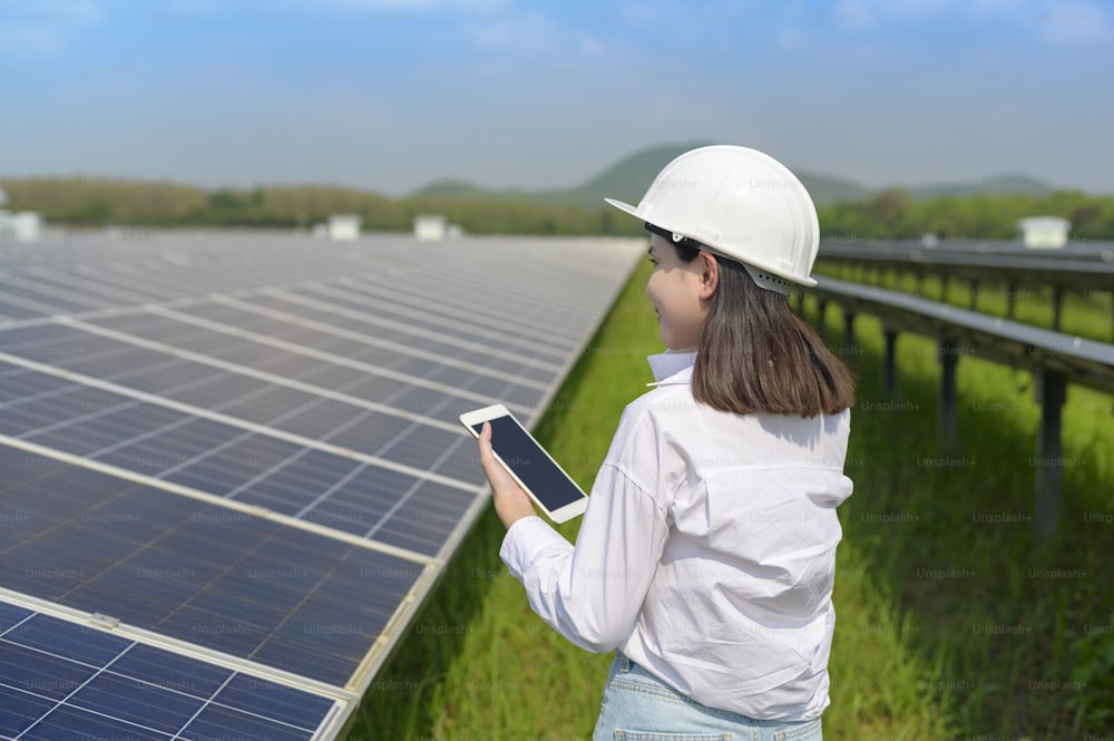 Eine Ingenieurin, die einen Helm in Photovoltaic Cell Farm oder Solar Panels Field trägt, umweltfreundliche und saubere Energie.
