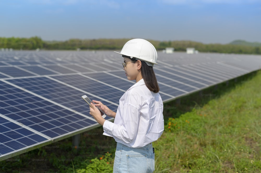 A female engineer wearing helmet in Photovoltaic Cell Farm or Solar Panels Field, eco friendly and clean energy.