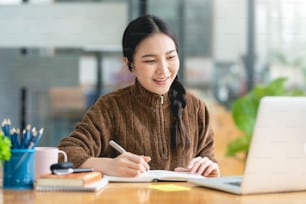 Pretty young Asian female student studying online on laptop computer.
