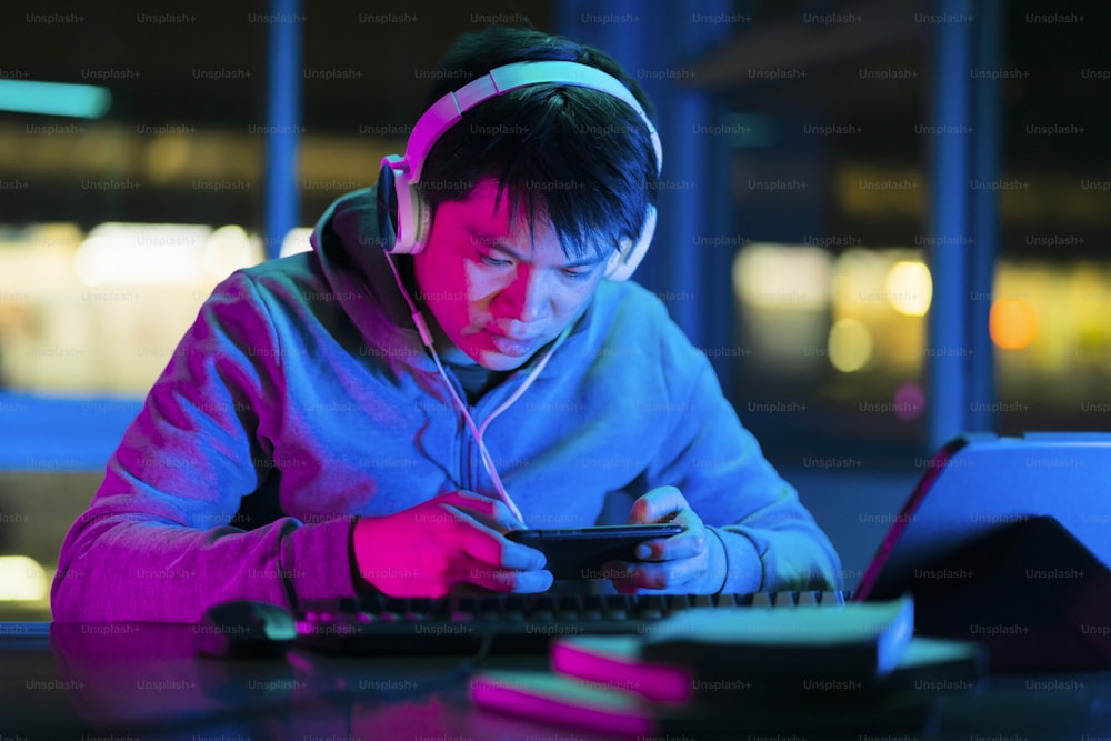 asian male esports gamer playing online sport leagues multiplayer game via smartphone with exited and cheerful emotion,asian male wear headset playing smartphone game online together with friends