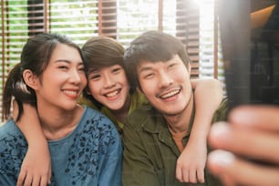 happiness asian family stay together at home using smartphone taking selfie pgoto or videocalling to their grandparent distancing communication,portrait of selfie family together in living room home