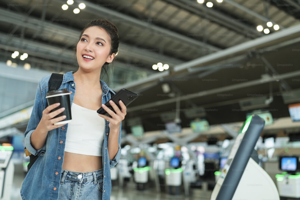 국외 거주자 디지털 유목민 여행 및 작업, 스마트폰 예약을 사용하는 동안 아시아 쾌활한 여성 캐주얼 천 걷기 공항 터미널에서 온라인 항공권 정보 응용 프로그램 여행 개념