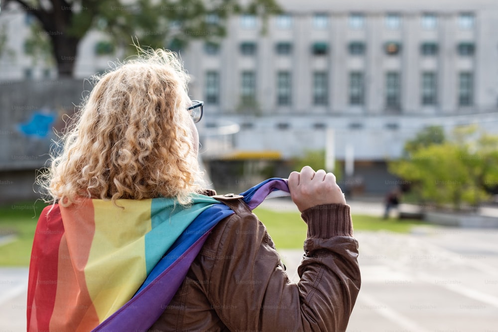 Vista posteriore o un'attivista lesbica sotto la bandiera arcobaleno LGBT. Concetto di orgoglio. Orgoglio