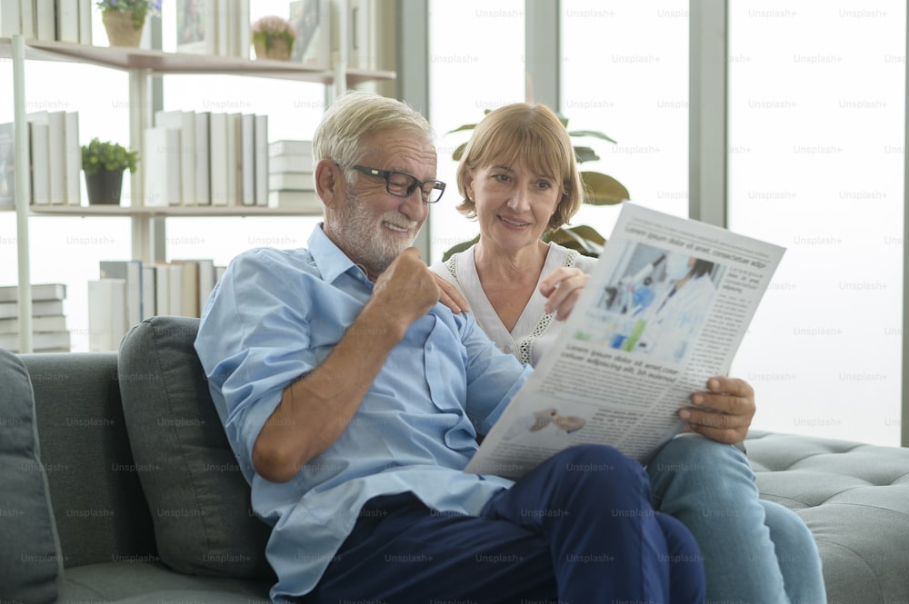 Casal feliz Caucasiano sênior estão relaxando, lendo jornal na sala de estar