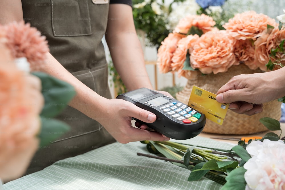 Hand des Kunden bezahlt mit kontaktloser Kreditkarte im Blumenladen