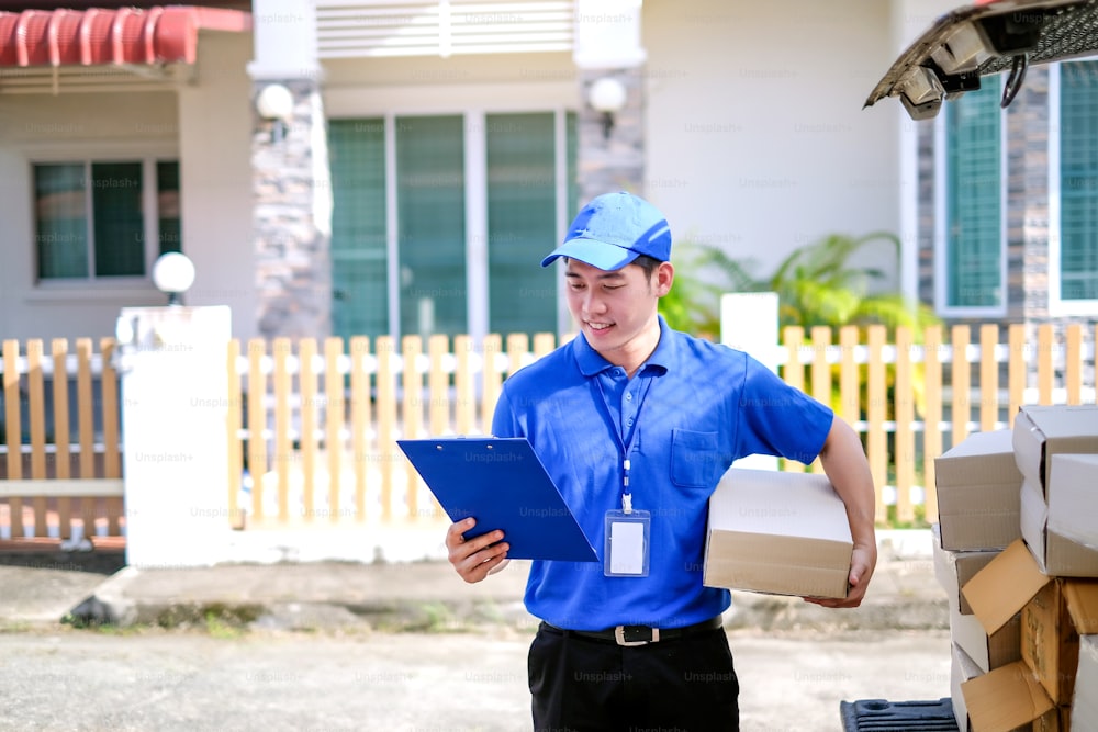 Young delivery man in blue uniform checking product boxes to send to customers on transportation vehicles.