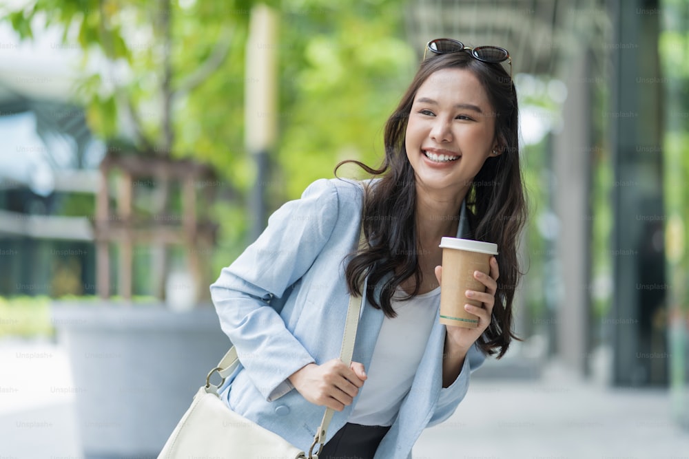Asiatische weibliche lässige entspannen digitale Nomadin freiberufliche Expat-Programmiererin Smart Casual Stoff Gehen auf Bürgersteig Stadt mit Kaffeetasse lächeln fröhlich positives Gefühl herunterschalten Lebensstil
