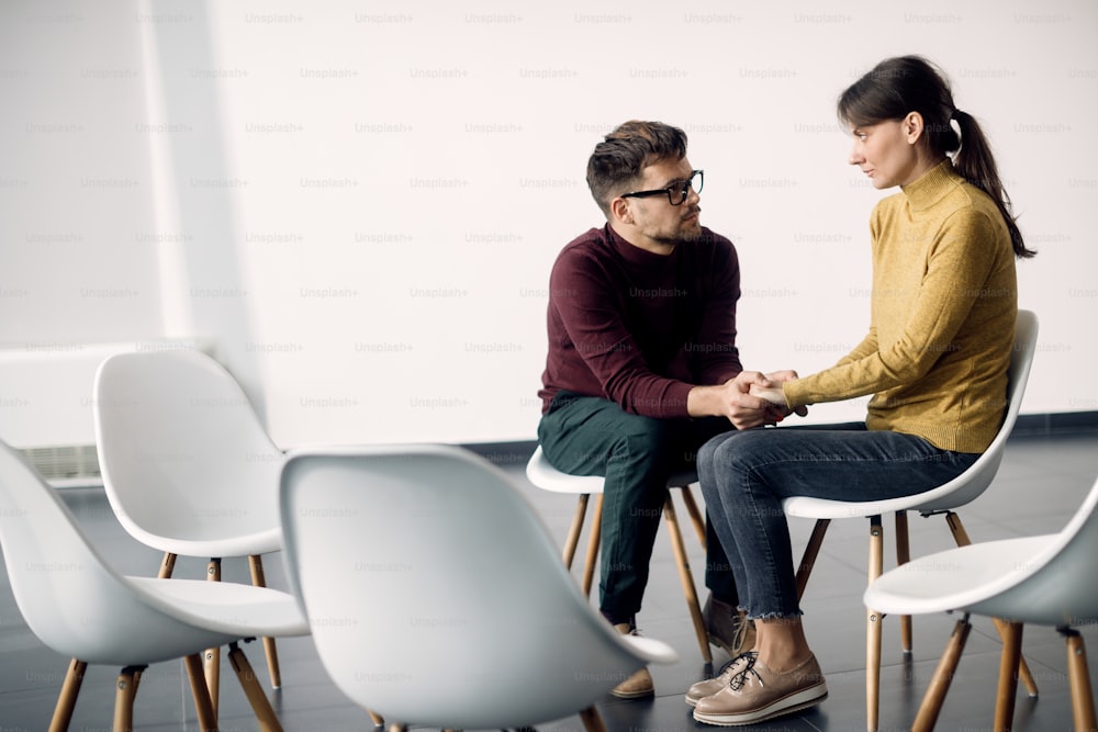 Young distraught couple holding hands while waiting for the group therapy to start. Copy space.