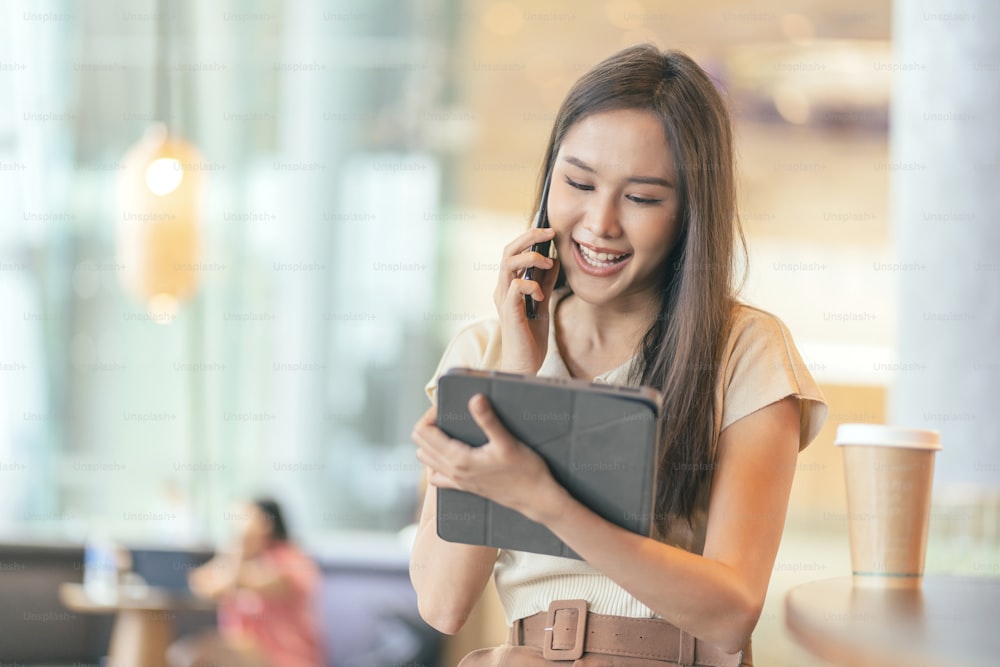 똑똑한 매력적인 아시아 여성 여성 캐주얼 천 프리랜서 작업 레저 휴식 카페 레스토랑에서 노트북과 스마트폰으로 작업 도시 라이프스타일 공동 작업 공간에서 일하는 디지털 유목민