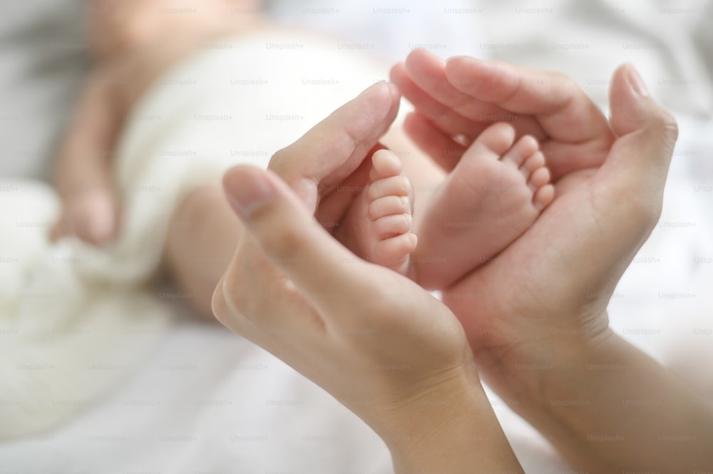 Enge Hand, die die Füße des Neugeborenen hält