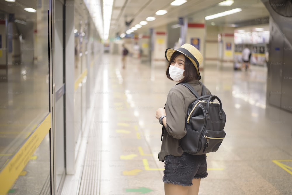 若いかわいいアジアの女性が地下鉄駅に立って保護マスクを着用しています、ニューノーマル旅行、covid-19保護、安全な旅行、COVID-19下での旅行、パンデミック後の旅行コンセプト。