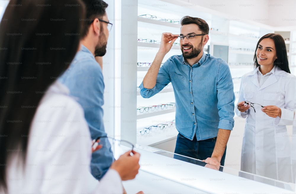 La joven oftalmóloga doctora está ayudando a un hombre guapo a elegir las gafas más adecuadas. Médico y paciente en una moderna clínica oftalmológica