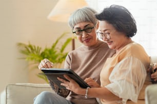 Visite de la maison de deux vieilles amies matures âgées regardant à travers de vieilles photos album numérique avec tablette sur le canapé dans le salon à la maison vieil ami Passer du temps de qualité ensemble