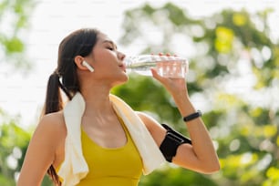 giovane donna che beve acqua dalla bottiglia. femmina asiatica che beve acqua dopo esercizi o sport. Bella donna atleta di fitness che indossa acqua potabile del cappello dopo l'esercizio di esercizio la sera del tramonto