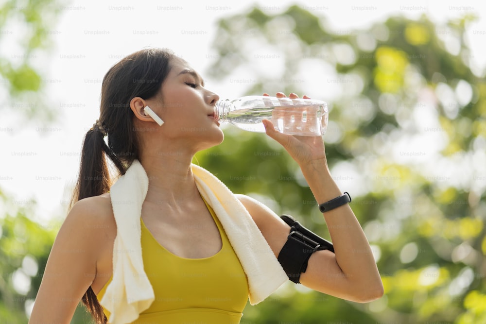 Mujer joven bebiendo agua de botella. Mujer asiática bebiendo agua después de hacer ejercicio o deporte. Hermosa mujer atleta de fitness con sombrero bebiendo agua después de hacer ejercicio en la noche del atardecer