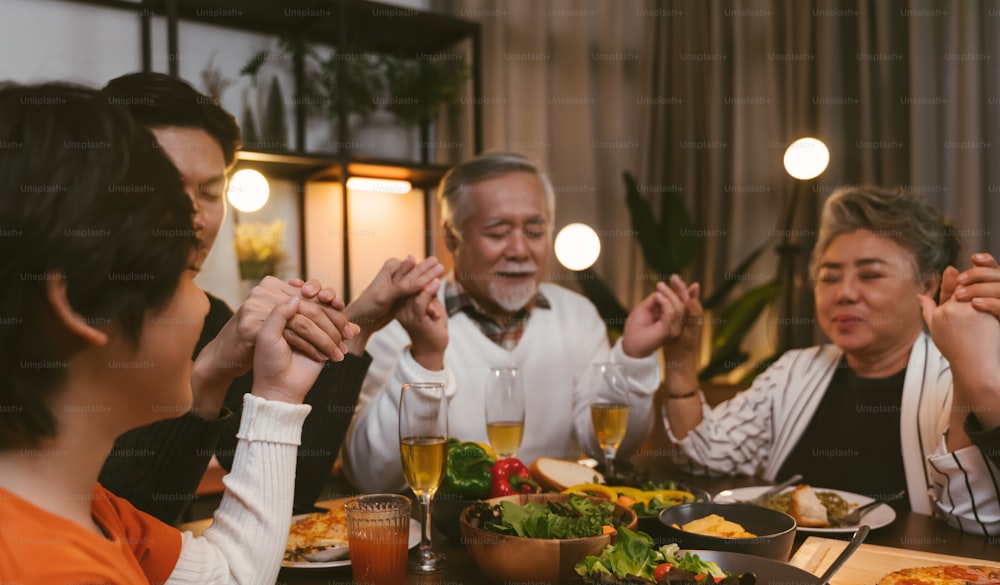 Grande família asiática fechando os olhos ao dizer graça orando antes de jantar em casa