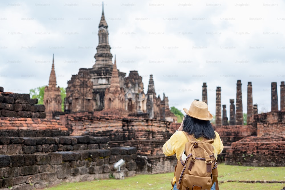 Asian tourist woman take a photo of ancient of pagoda temple thai architecture at Sukhothai Historical Park,Thailand. Female traveler in casual thai cloths style visiting city concept.
