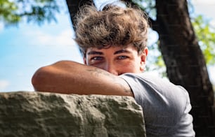 Young man falls his head down on his arms, smiling and looking at the camera in a public park