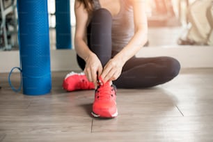 Pretty young sport woman is tying her sneakers in gym, Healthy lifestyle
