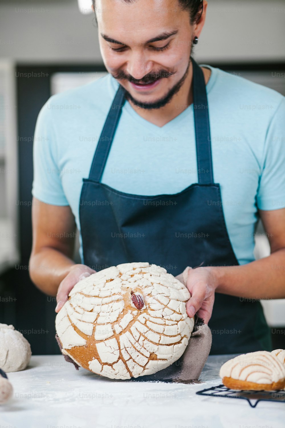 portrait of Latin man standing in kitchen baking and holding Conchas traditional Mexican bread in Mexico city