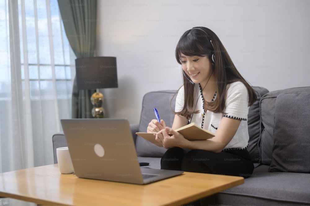 헤드셋을 착용한 아름다운 젊은 여성이 집에서 컴퓨터를 통해 화상 회의를 하고 있다