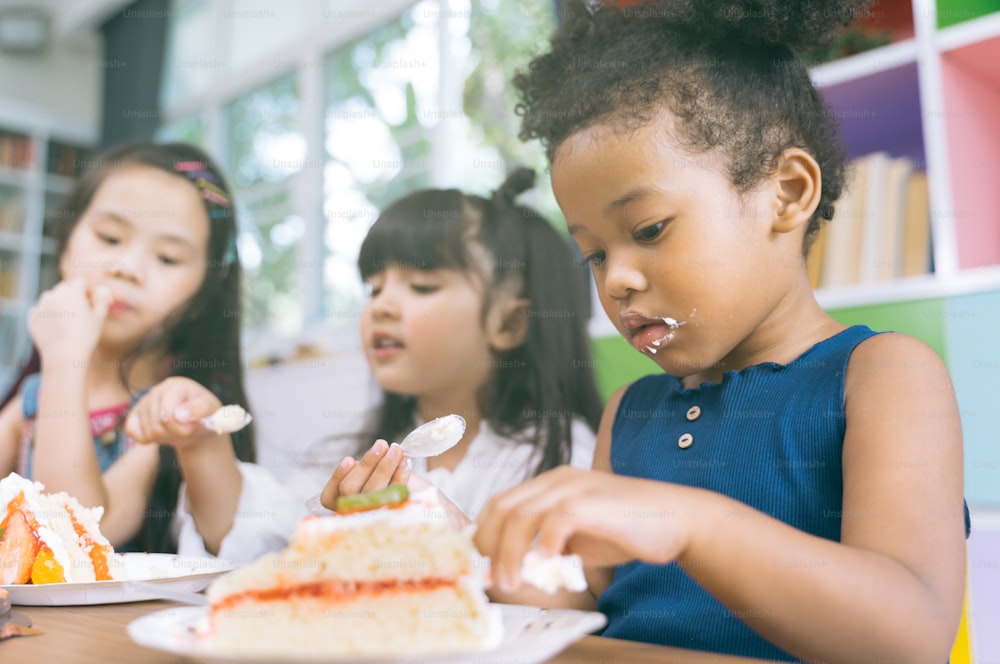 linda niña con amigos de la diversidad comiendo pastel juntos. Los niños comen postre.