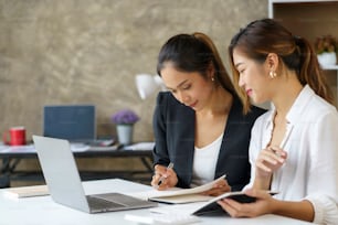 Two young Asian professional businesswomen working talking in a modern startup.