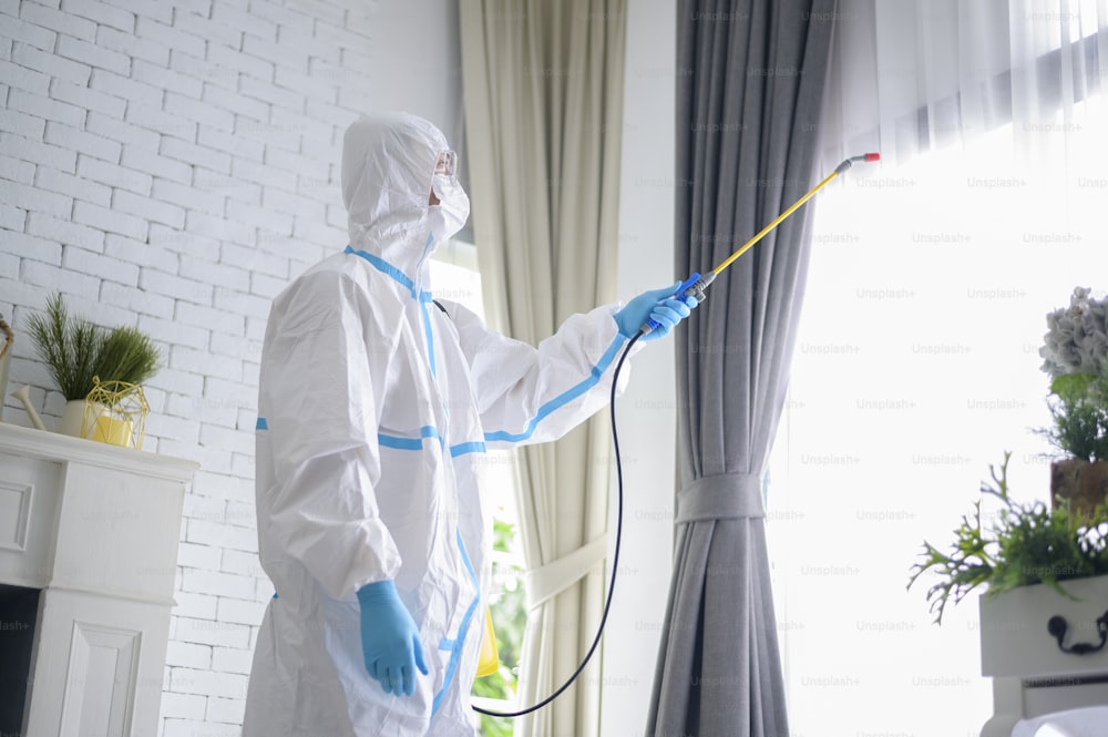 Uma equipe médica em traje de EPI está usando spray desinfetante na sala de estar, proteção contra a Covid-19, conceito de desinfecção.