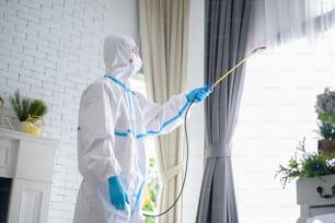 A medical staff in PPE suit is using disinfectant spray in living room, Covid-19 protection , disinfection concept .