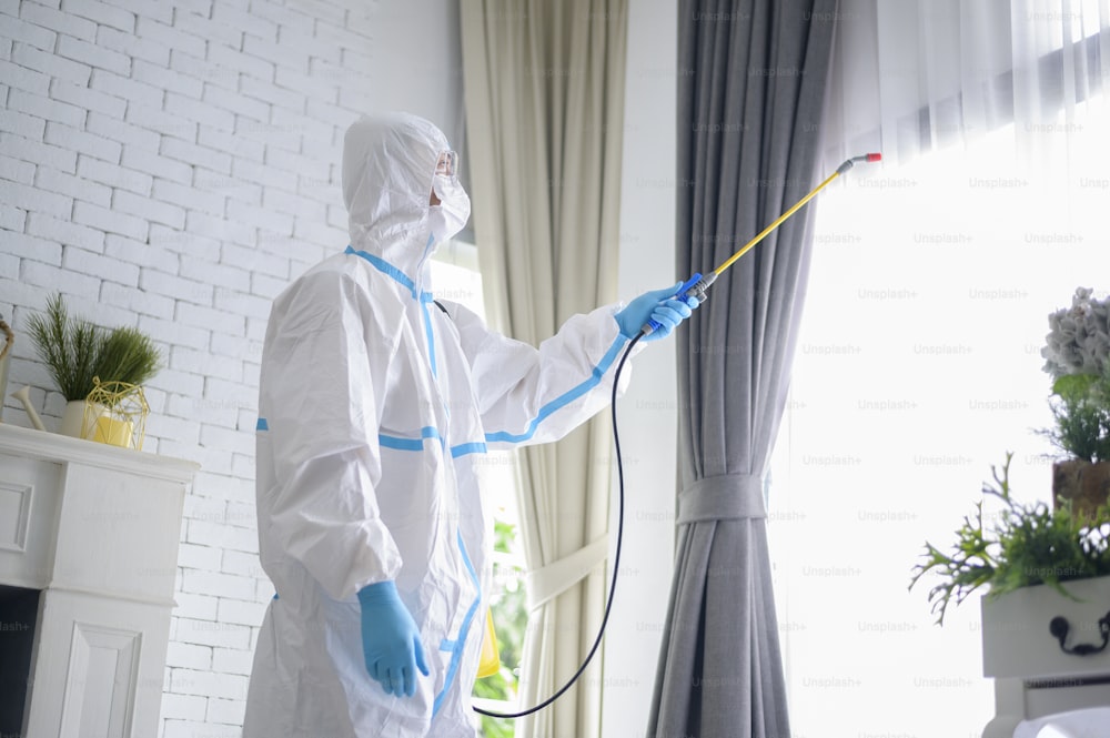 A medical staff in PPE suit is using disinfectant spray in living room, Covid-19 protection , disinfection concept .