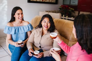 Chicas latinas divirtiéndose en casa, riendo y tomando café en la ciudad de México