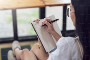 Close-up de uma mão de mulher segurando uma caneta com um caderno tomando nota conceito.
