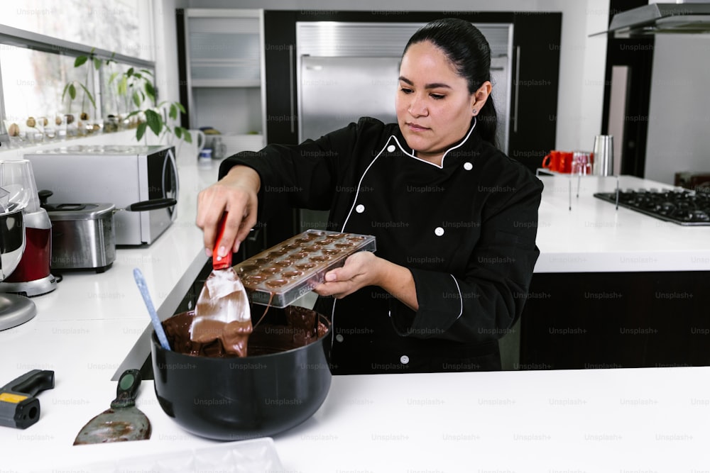 メキシコのラテンアメリカのキッチンでおいしいお菓子のチョコレートを準備する過程で黒い制服を着たラテン系の女性パティシエ
