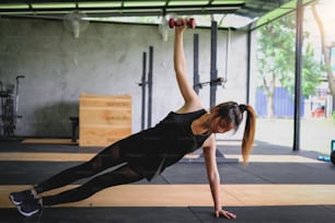 Young asian woman lifting a dumbbell during an exercise class at gym.