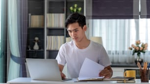 Young Asian man working on a laptop with document at home.