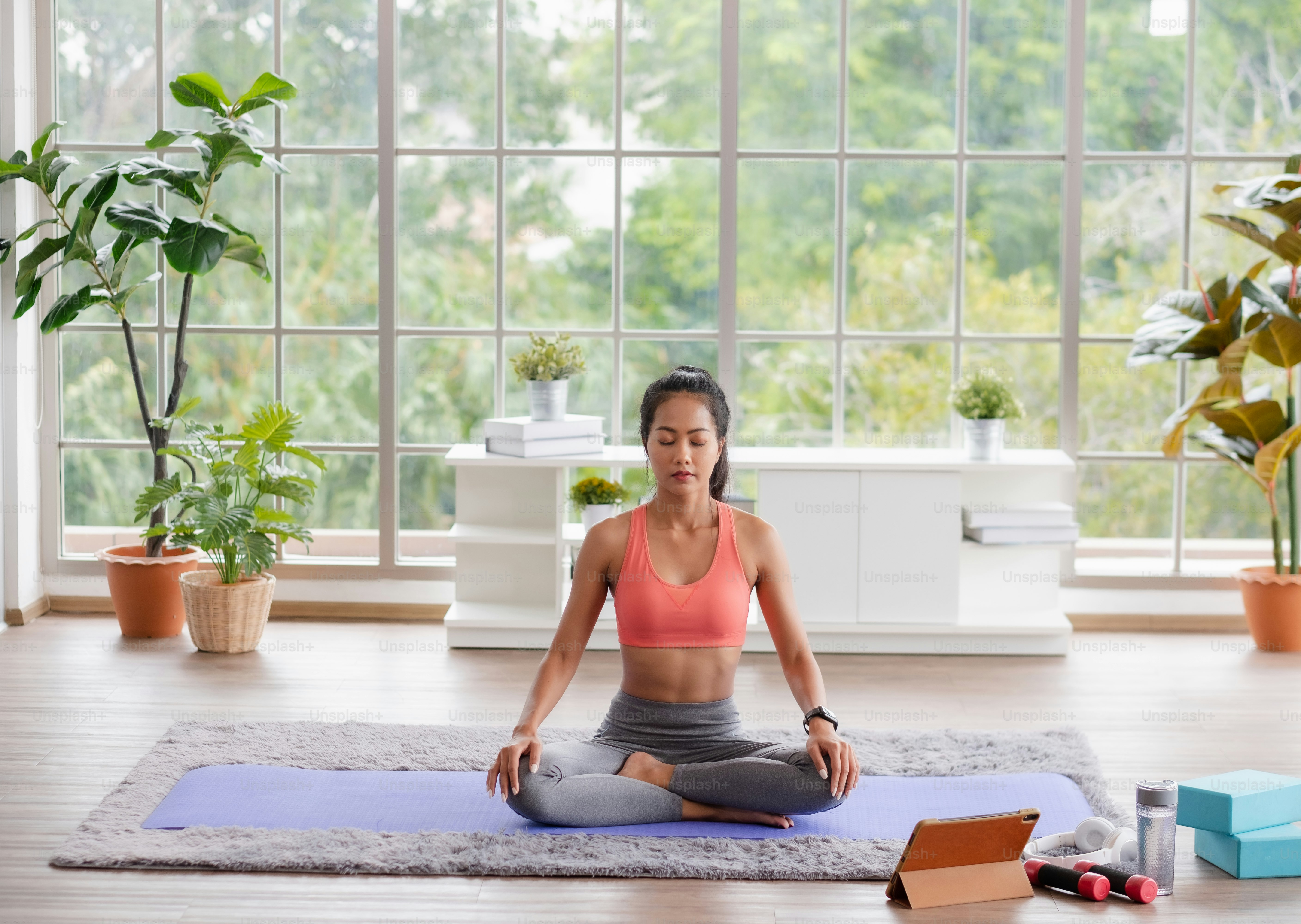 Young Asian woman in sportswear training yoga exercises with online video tutorial on tablet