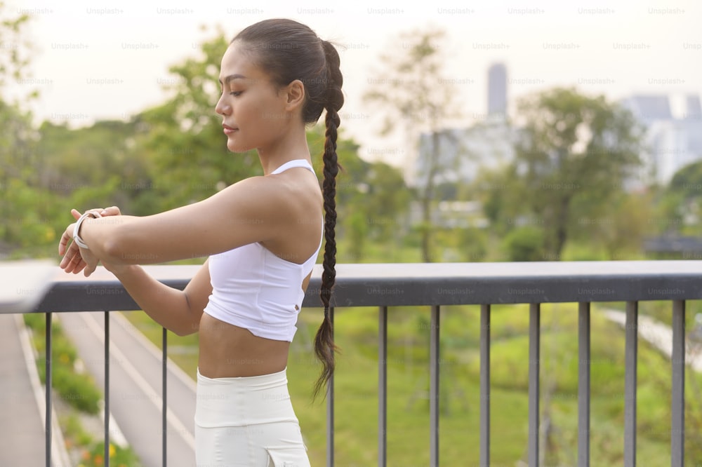 Una giovane donna di fitness in abbigliamento sportivo che utilizza un orologio intelligente mentre si esercita nel parco cittadino, Healthy and Lifestyles.
