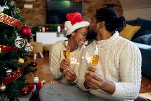Loving African American couple drinking Champagne and using sparklers while spending Christmas together at home.