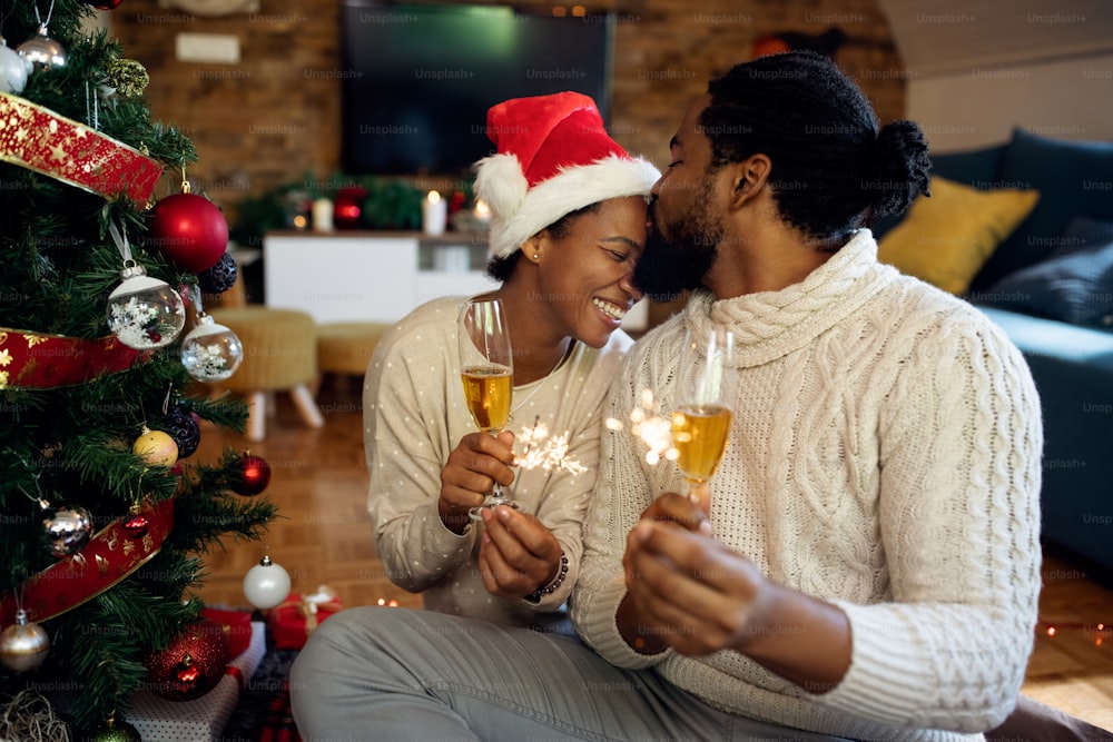 Loving African American couple drinking Champagne and using sparklers while spending Christmas together at home.