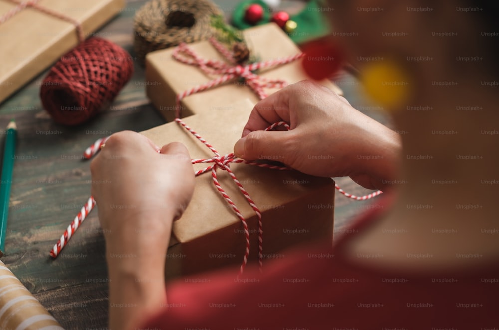 femme faisant une boîte-cadeau à la main de Noël avec du papier brun déformant avec un décor de Noël sur une table en bois