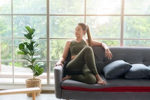 Una hermosa mujer asain en forma en ropa deportiva sentada y relajándose en el sofá después del entrenamiento, la salud y el concepto de ejercicio