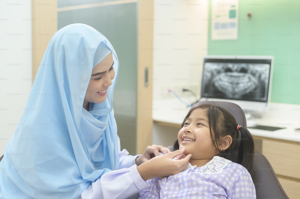 Una piccola ragazza carina che si fa esaminare i denti dal dentista musulmano in clinica dentale, controllo dei denti e concetto di denti sani