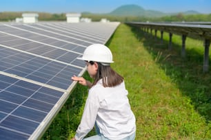 A female engineer wearing helmet in Photovoltaic Cell Farm or Solar Panels Field, eco friendly and clean energy.