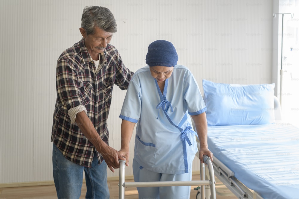 病院、医療、医療コンセプトで歩行器でヘッドスカーフをかぶったがん患者の女性を助ける高齢者の男性
