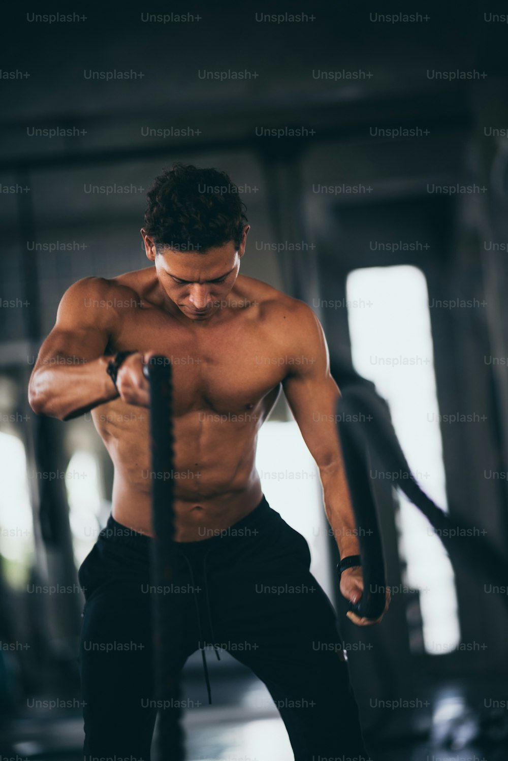 Homem agressivo poderoso muscular treinando com corda em academia de fitness de treinamento funcional