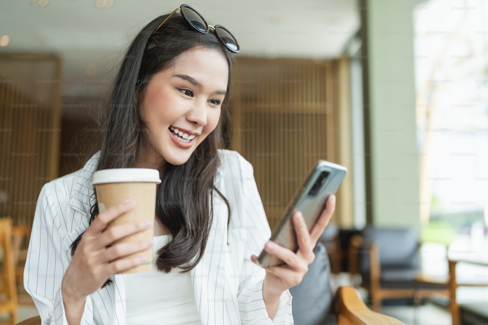 atractiva inteligente casual asiática femenina que escribe a mano chat usando la telecomunicación del teléfono inteligente actitud positiva sonrisa en el café casual, empresario inteligente propietario de un negocio que trabaja con el teléfono inteligente en el café