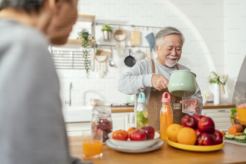 Group of senior friends having party indoors, cooking and talking positive conversation in senior daycare,asian Senior male standing in kitchen and relaxing at home while eating a healthy food recipe