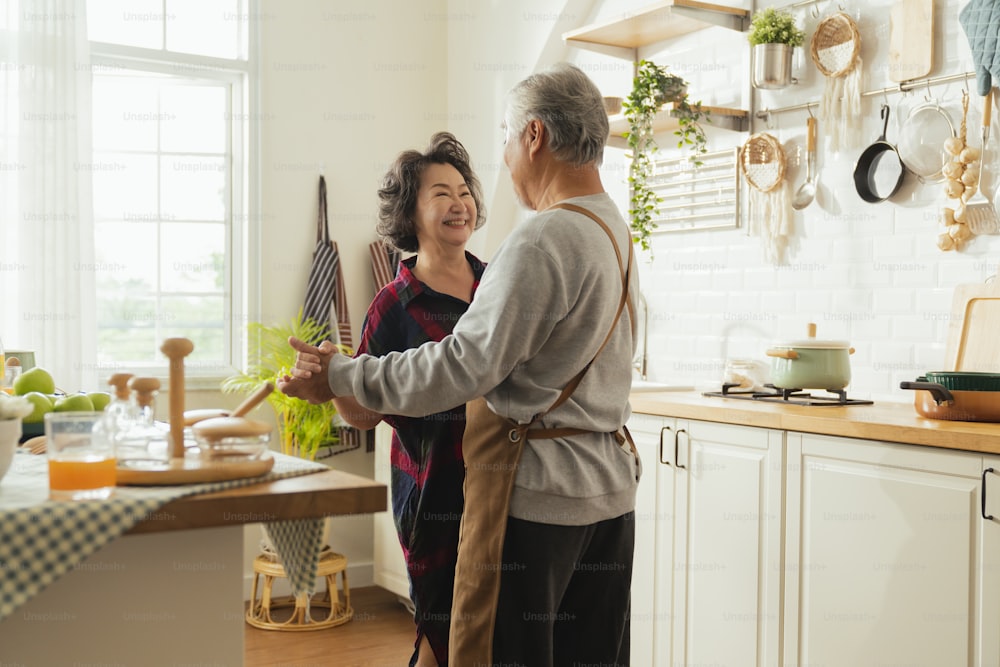 Pareja asiática de adultos mayores cocinando comida saludable juntos en casa mientras bailan en la cocina por la mañana fin de semana, felicidad pareja asiática de matrimonio de ancianos disfruta de una romántica toma recortada de una pareja mayor bailando